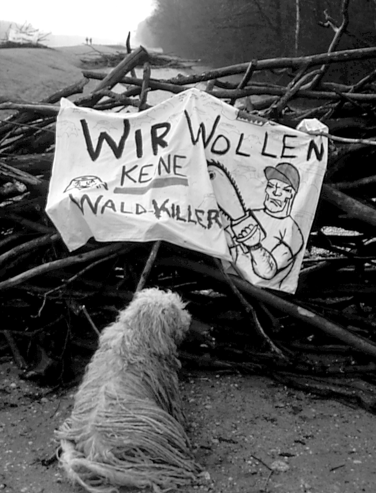Hund sitzt vor einer Barikade mit der Aufschrift: Wir wollen keine Waldkiller
